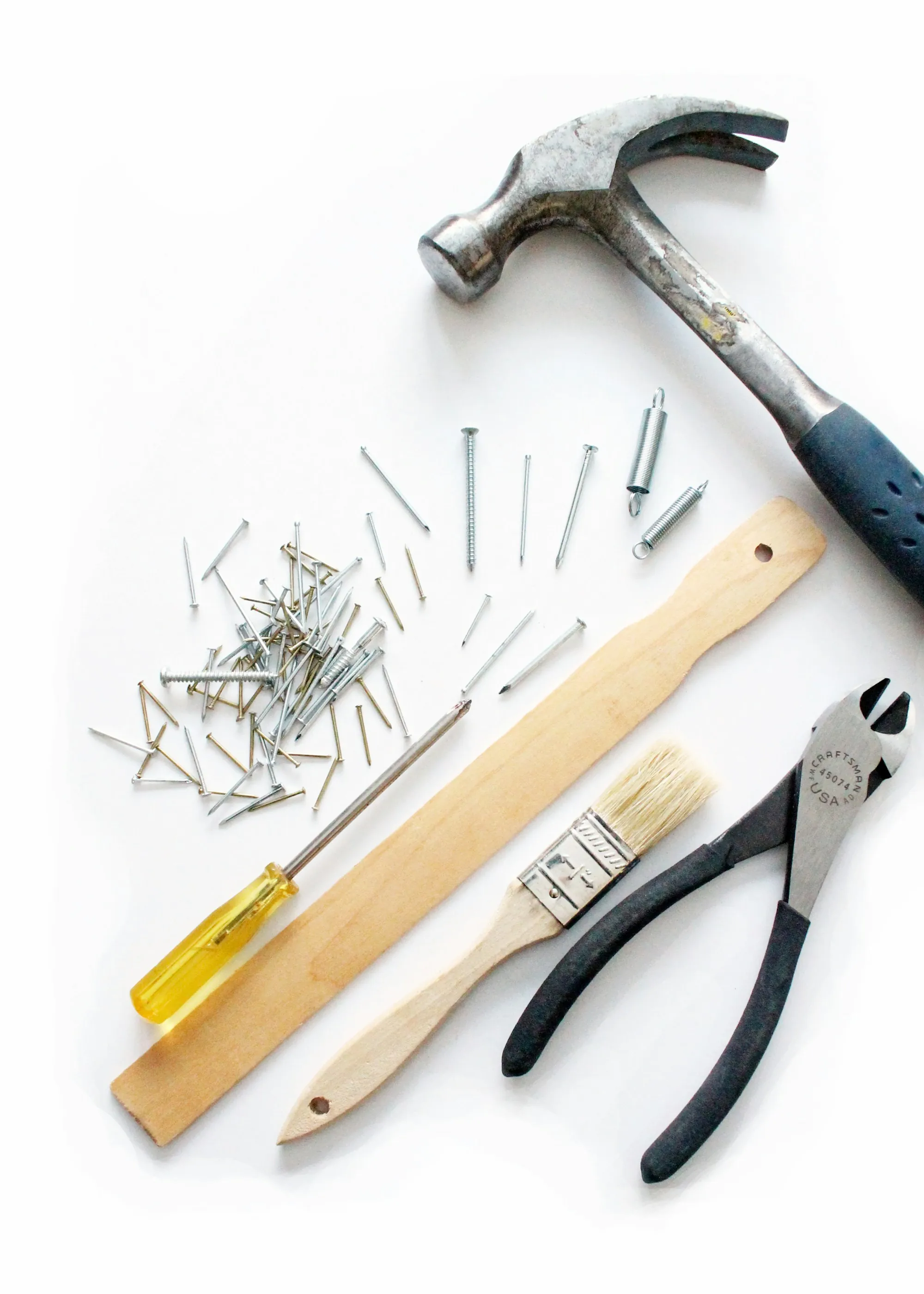 Screwdriver, pliers and nails laid out on a white surface